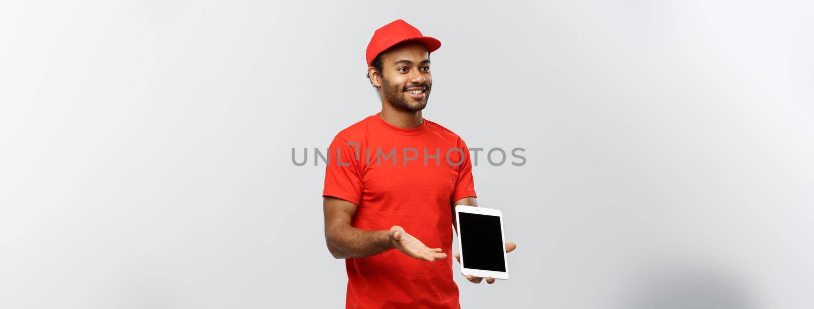 Delivery Concept - Portrait of Handsome African American delivery man or courier showing tablet on you to check the order. Isolated on Grey studio Background. Copy Space. by Benzoix