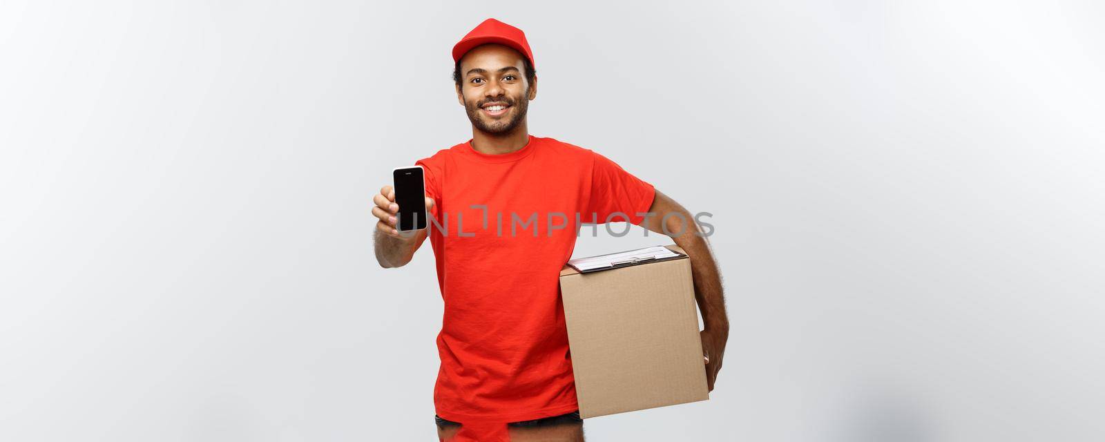 Delivery Concept - Portrait of Handsome African American delivery man or courier with box showing mobile phone on you to check the order. Isolated on Grey studio Background. Copy Space