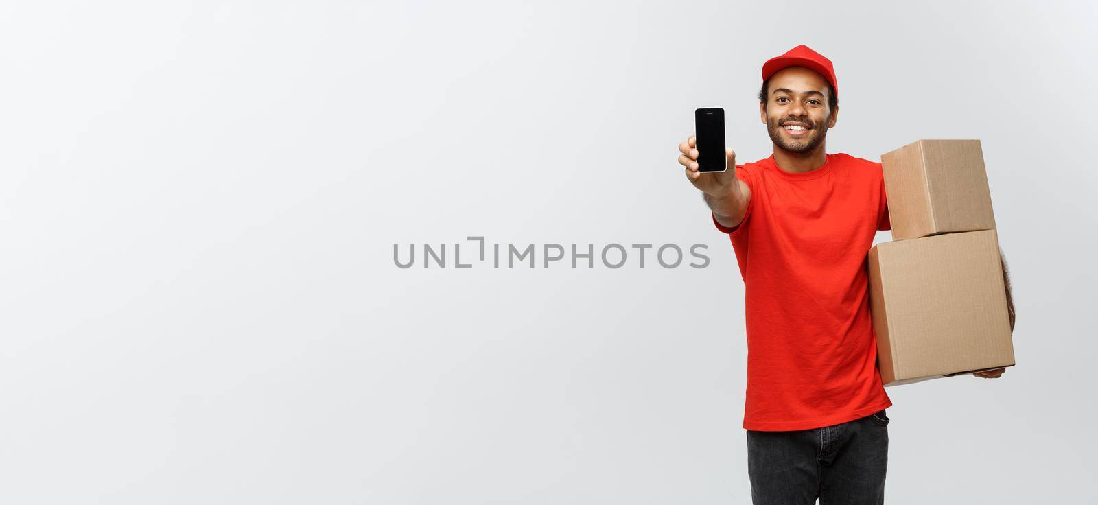 Delivery Concept - Portrait of Handsome African American delivery man or courier with box showing mobile phone on you to check the order. Isolated on Grey studio Background. Copy Space