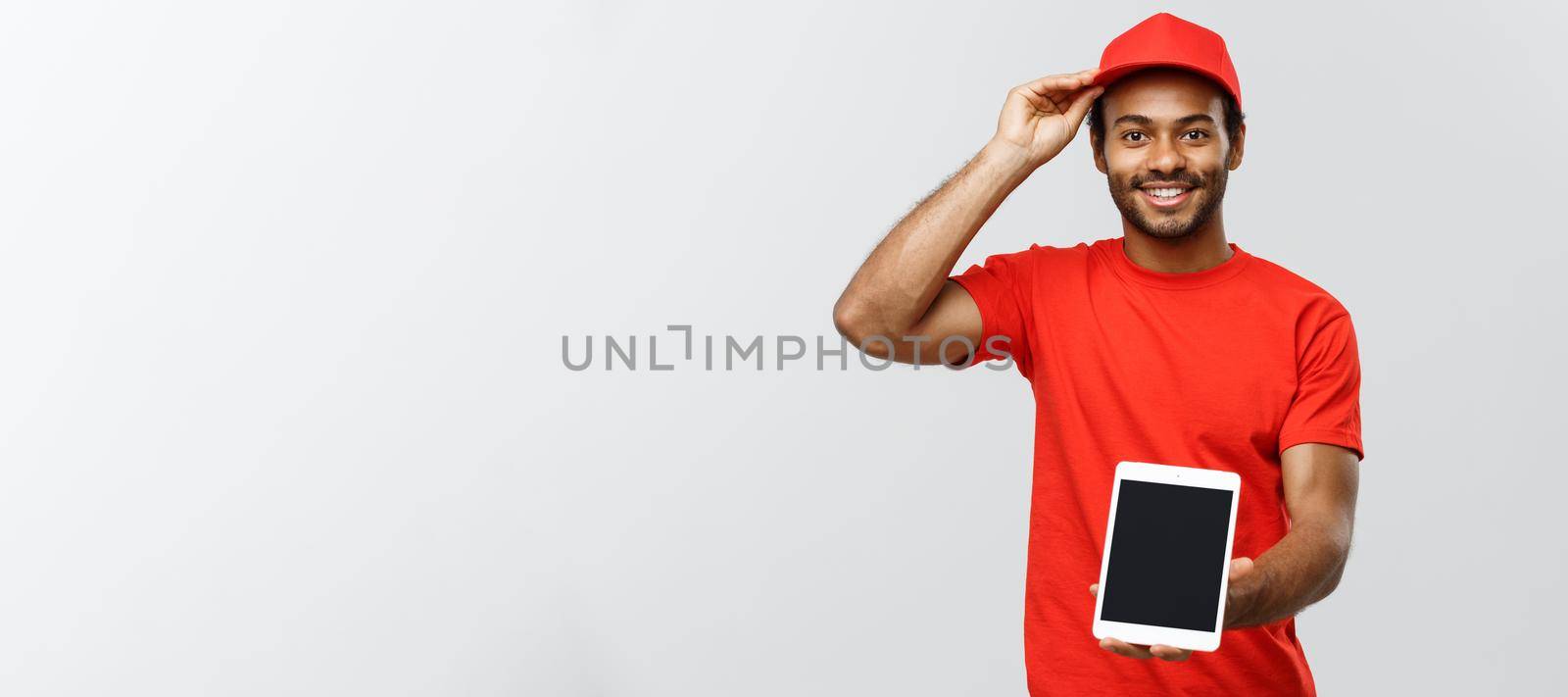 Delivery Concept - Portrait of Handsome African American delivery man or courier showing tablet on you to check the order. Isolated on Grey studio Background. Copy Space