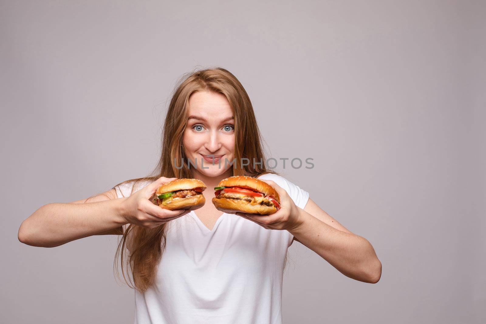 Close-up of unrecognizable brunette smiling woman holding two delicious fresh burgers with juicy roasted chicken and rocket salad.