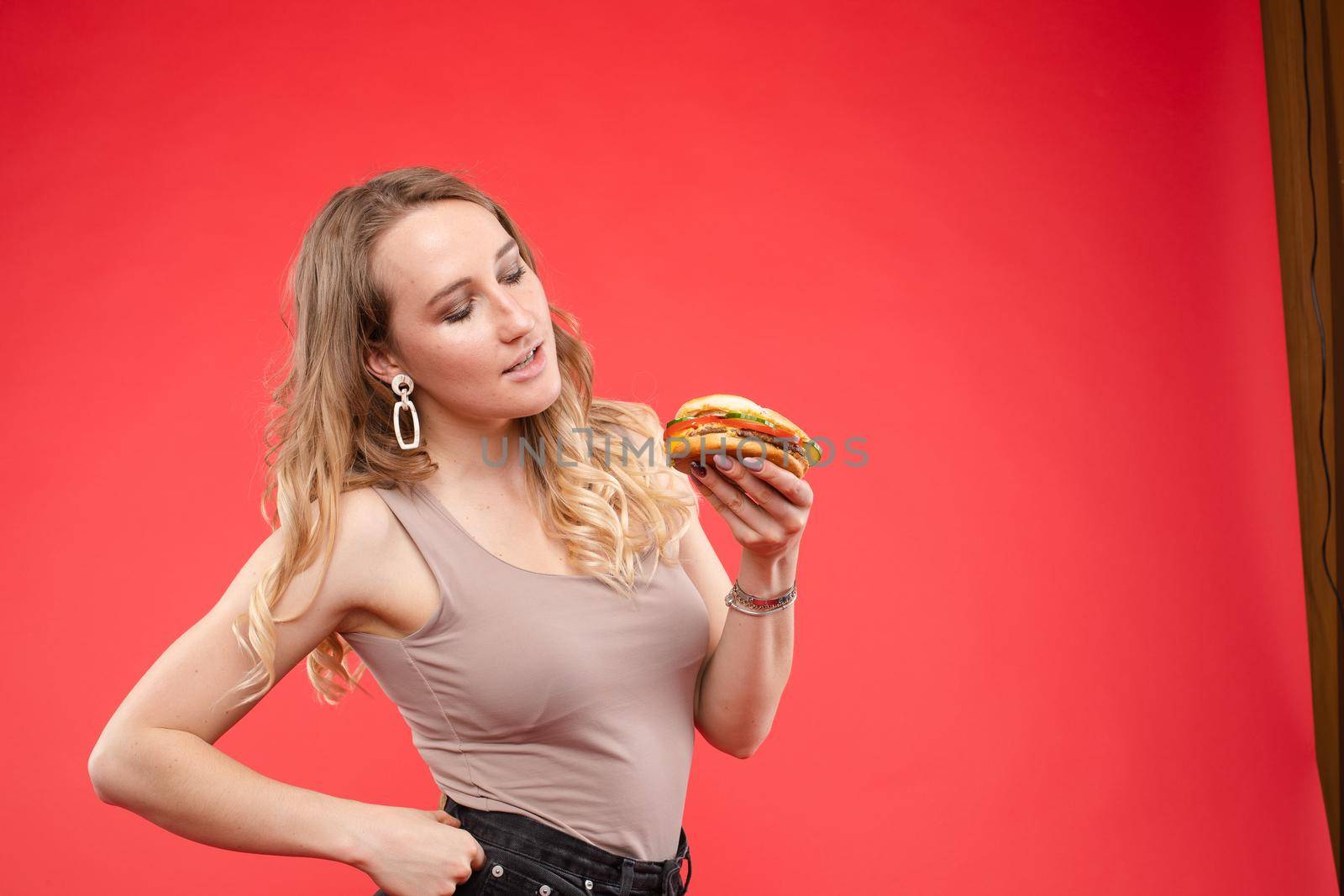 Medium close-up portrait of beautiful young fashion woman biting fresh appetizing sandwich by StudioLucky