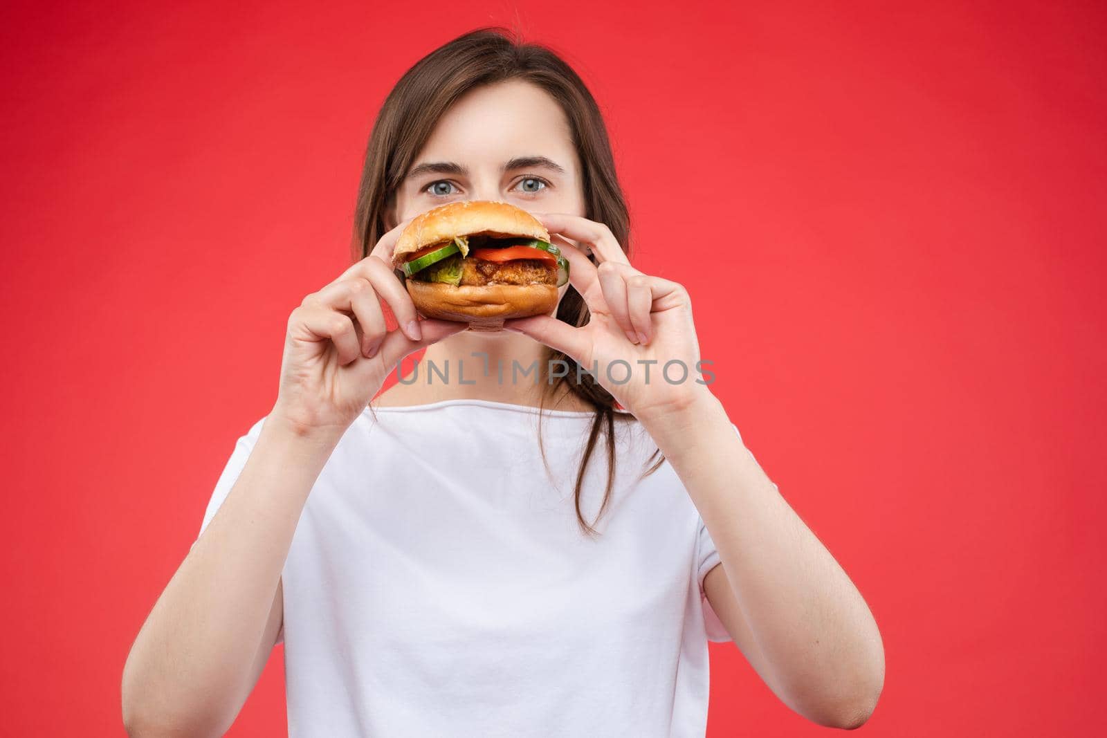 Medium close-up portrait of beautiful young fashion woman biting fresh appetizing sandwich by StudioLucky