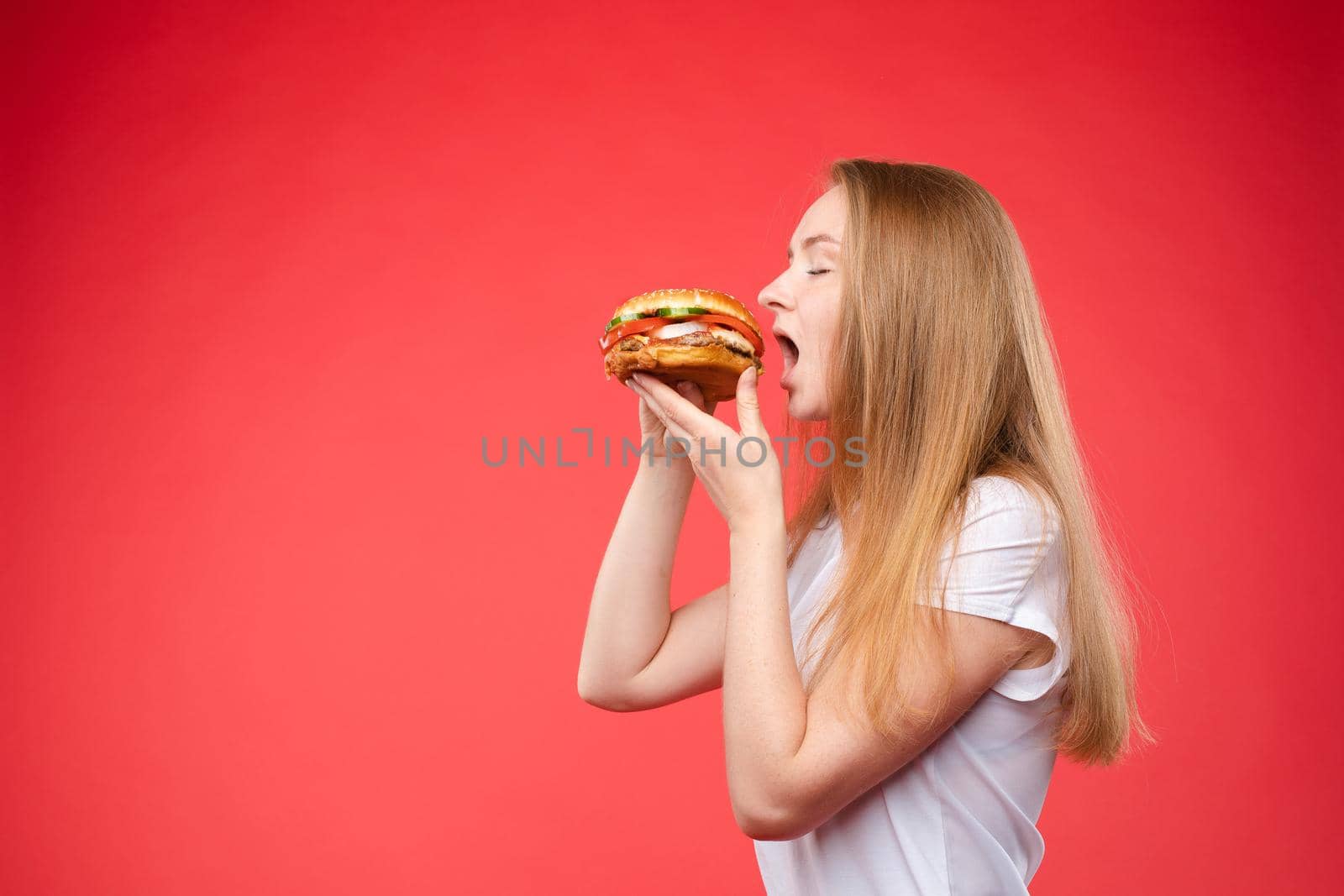 Medium close-up portrait of beautiful young fashion woman biting fresh appetizing sandwich by StudioLucky