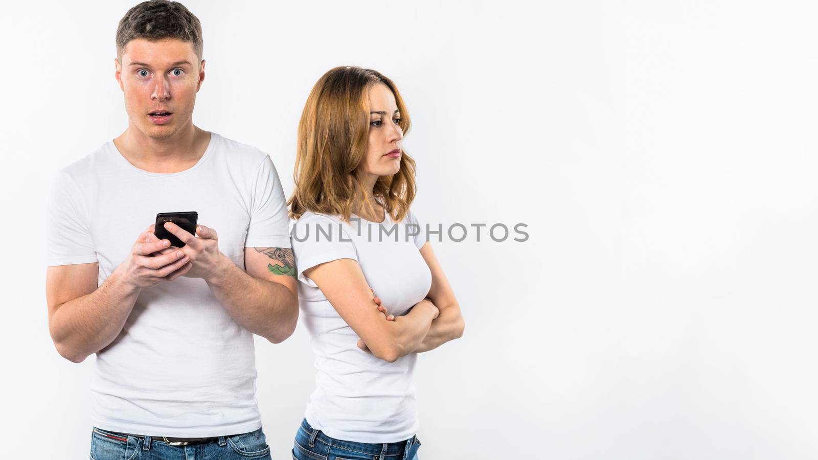 shocked man holding mobile phone hand standing near her angry girlfriend