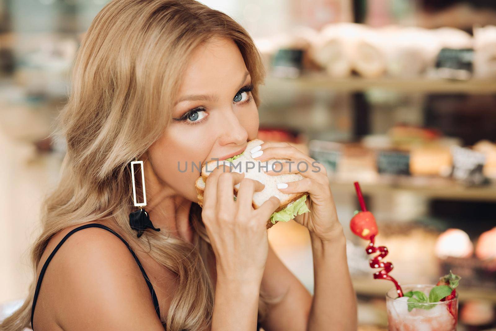 Attractive woman eating delicious sandwich in cafe by StudioLucky