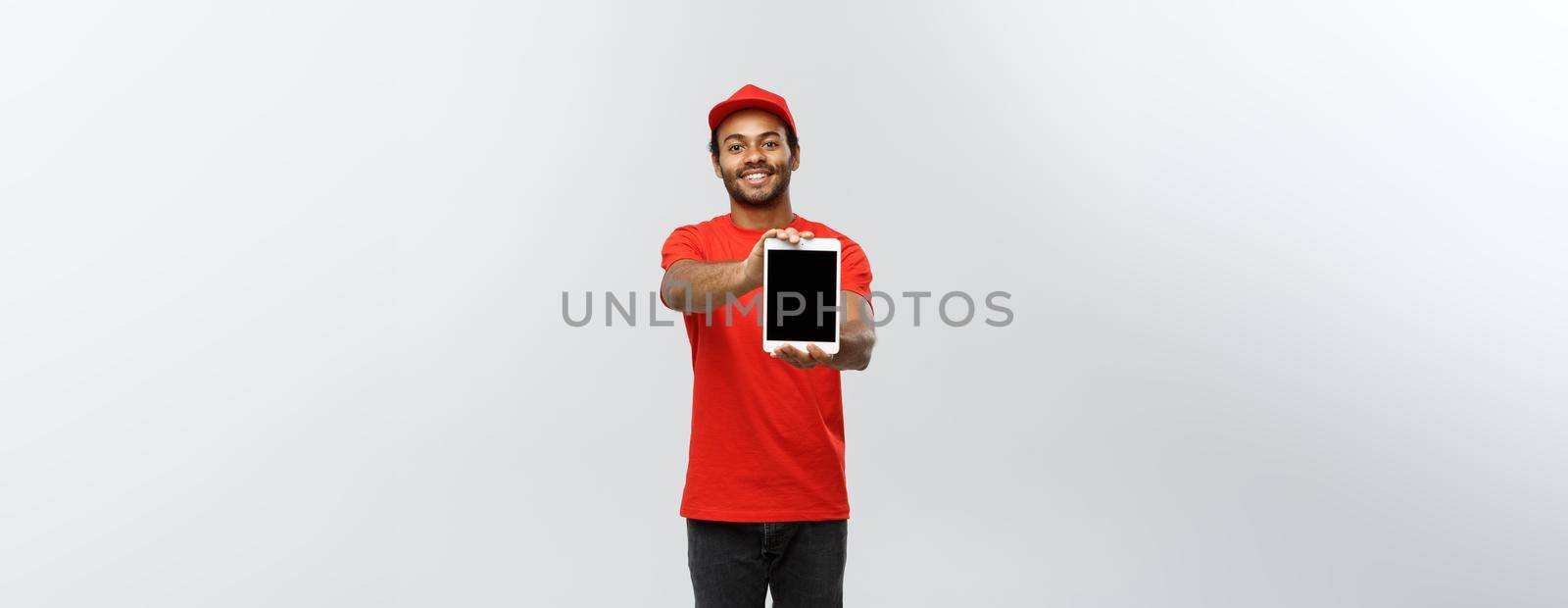 Delivery Concept - Portrait of Handsome African American delivery man or courier showing tablet on you to check the order. Isolated on Grey studio Background. Copy Space