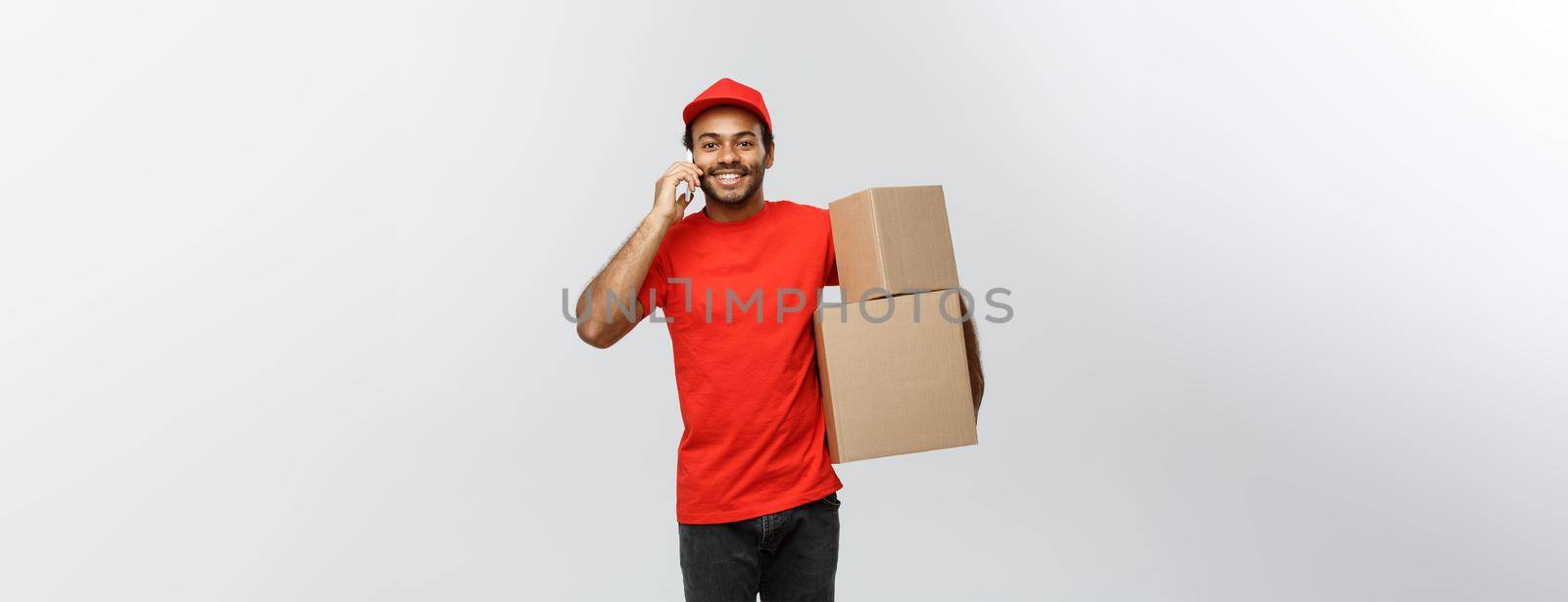 Delivery Concept - Portrait of Handsome African American delivery man or courier with box calling phone to customer. Isolated on Grey studio Background. Copy Space. by Benzoix