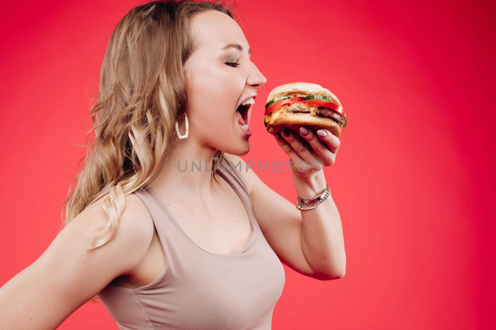 Medium close-up portrait of beautiful young fashion woman biting fresh appetizing sandwich by StudioLucky