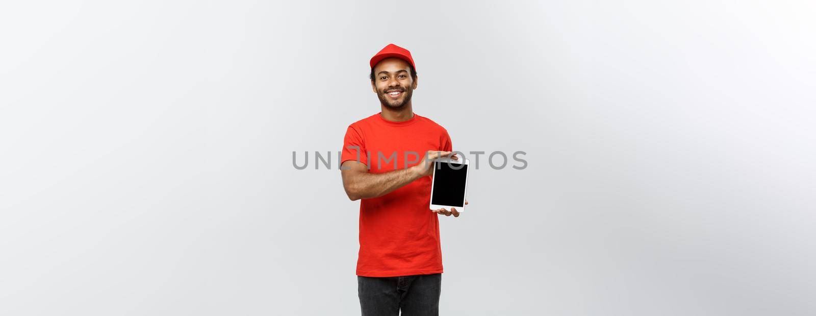 Delivery Concept - Portrait of Handsome African American delivery man or courier showing tablet on you to check the order. Isolated on Grey studio Background. Copy Space. by Benzoix