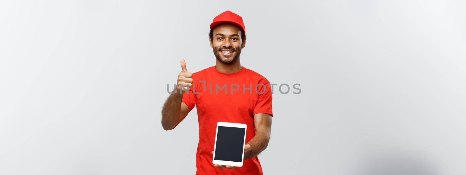 Delivery Concept - Portrait of Handsome African American delivery man or courier showing tablet on you to check the order. Isolated on Grey studio Background. Copy Space