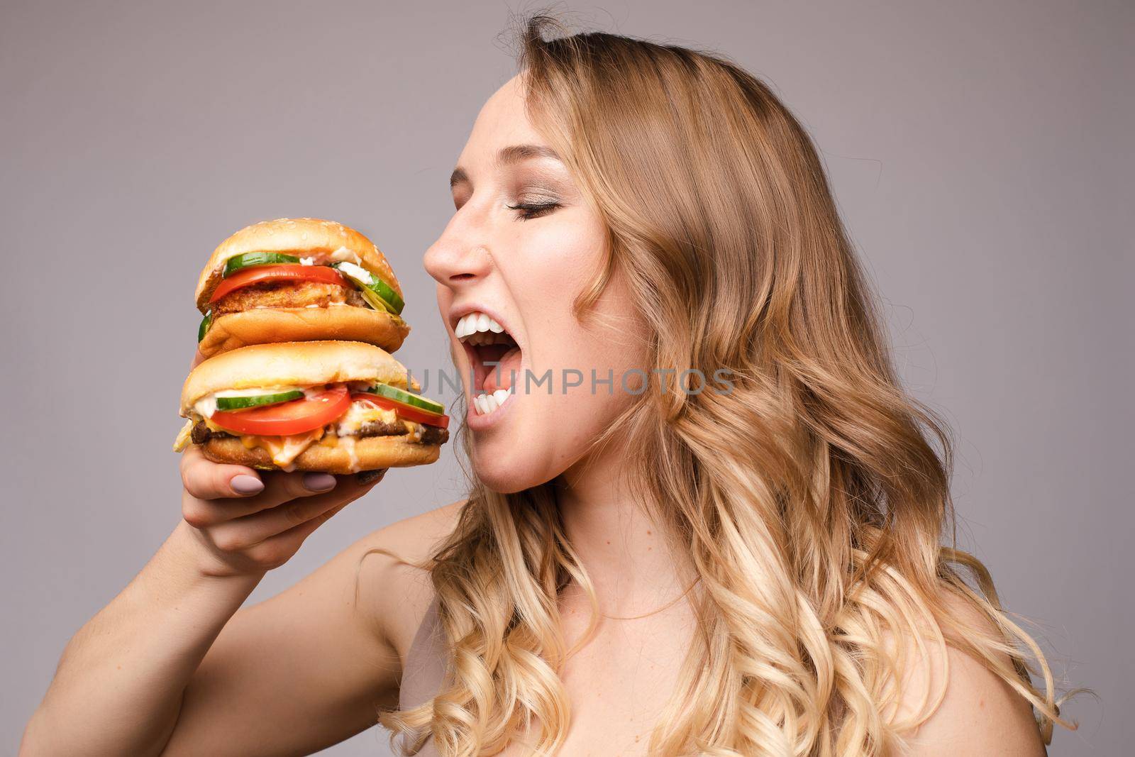 The woman opened her mouth to eat a hamburger by StudioLucky