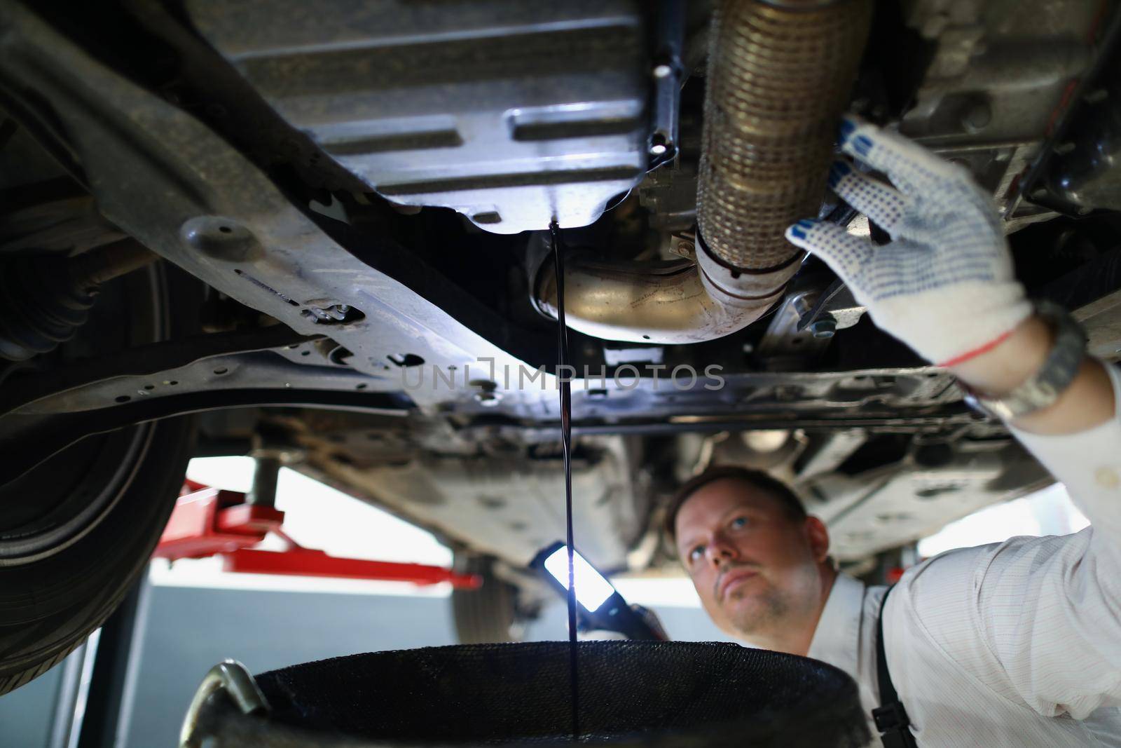 Portrait of mechanic man change oil under auto, car maintenance service, oil dripping. Qualified worker fix your vehicle. Pit stop, repair, service concept