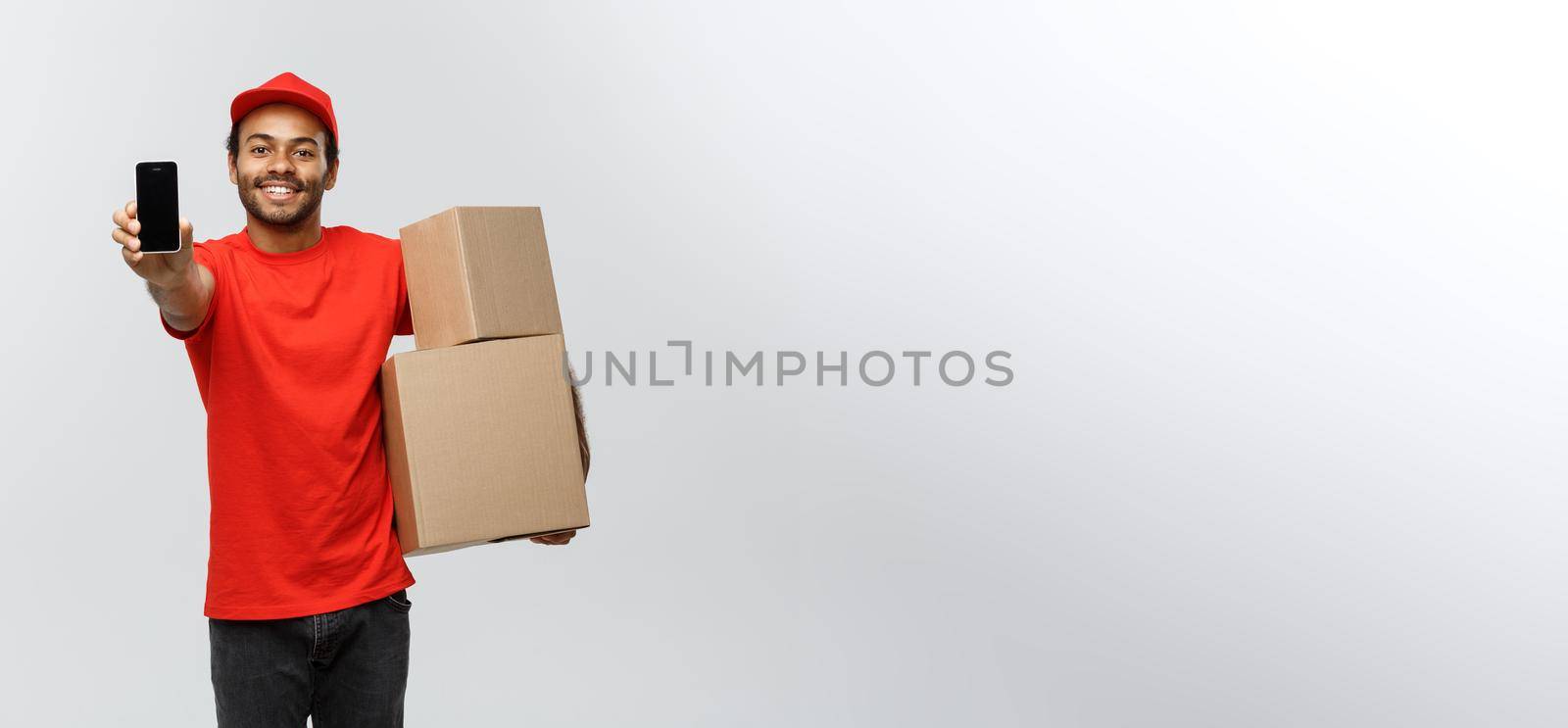 Delivery Concept - Portrait of Handsome African American delivery man or courier with box showing mobile phone on you to check the order. Isolated on Grey studio Background. Copy Space