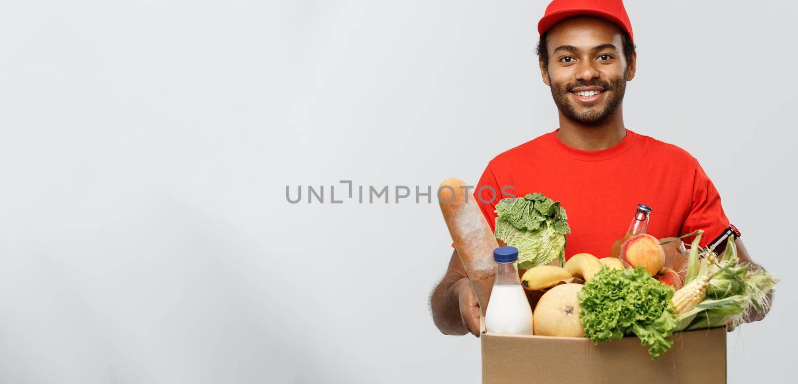 Delivery Concept - Handsome African American delivery man carrying package box of grocery food and drink from store. Isolated on Grey studio Background. Copy Space