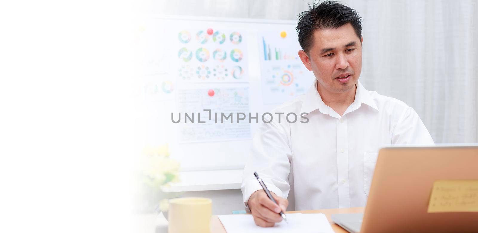 Asian businessman talking with team via video conference writing note on paper. business people using laptop  for online meeting. Business work from home concept.