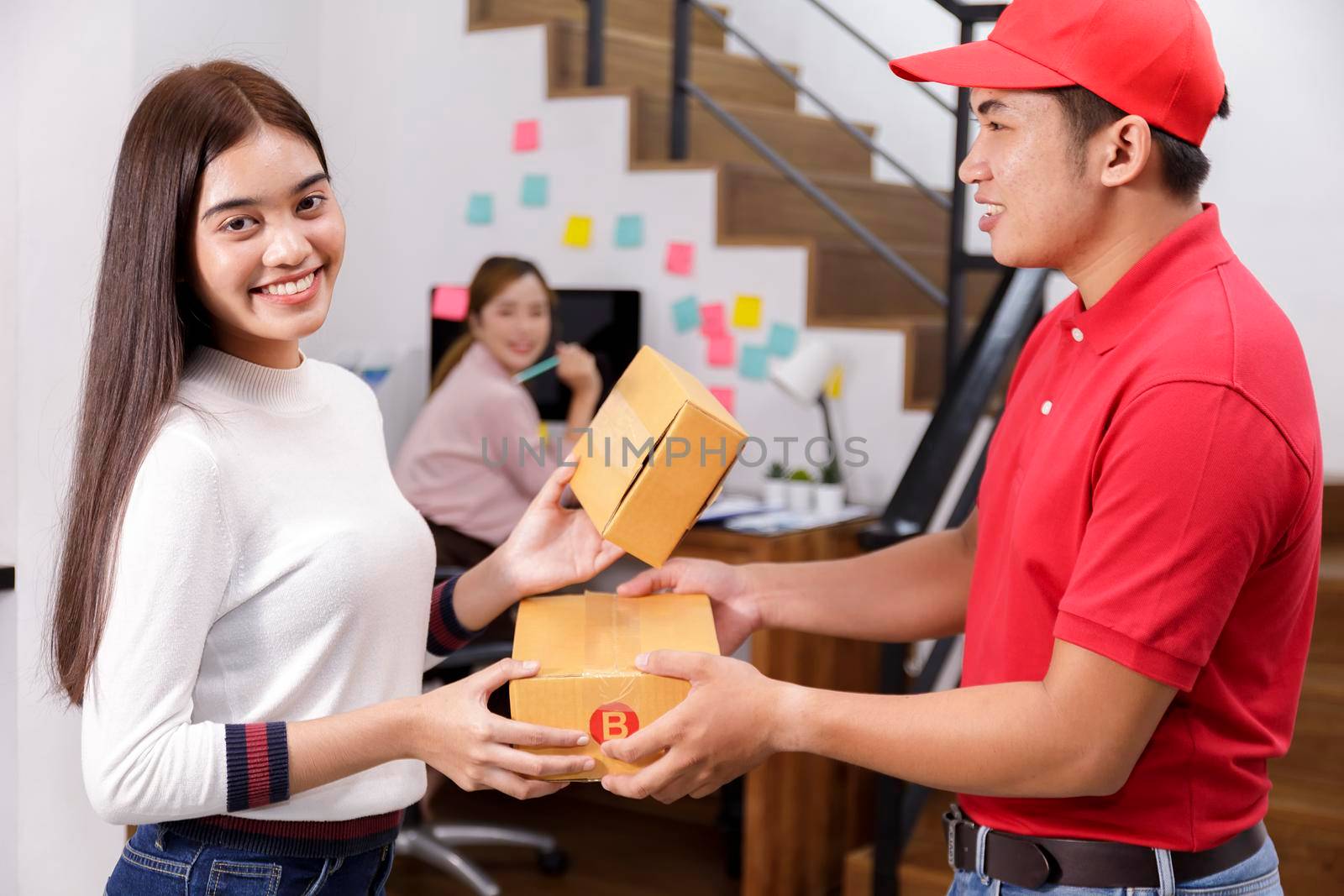 Delivery man delivering package to homeowner. Woman accepting a delivery of boxes from deliveryman. Delivery man wear red uniform sent box package to women. Delivery concept. by Satrinekarn