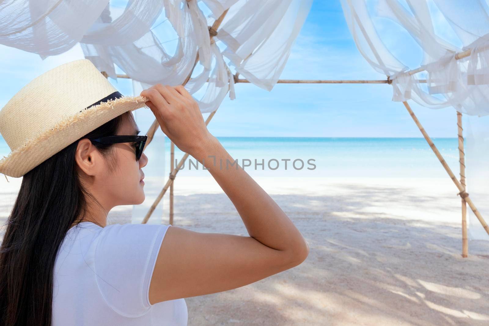 Portrait  middle shot view of woman stand in white T shirt and hat looking out towards blue ocean and sky, Women enjoy with beautiful sea view. Summer holiday vacation time