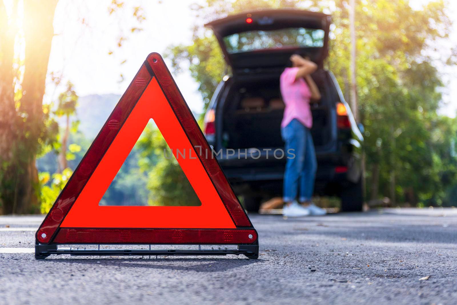 Close up red emergency stop sign standing on road. Worried and angry woman walking near his broken car talking on phone with insurance agent. Close up triangle on side road