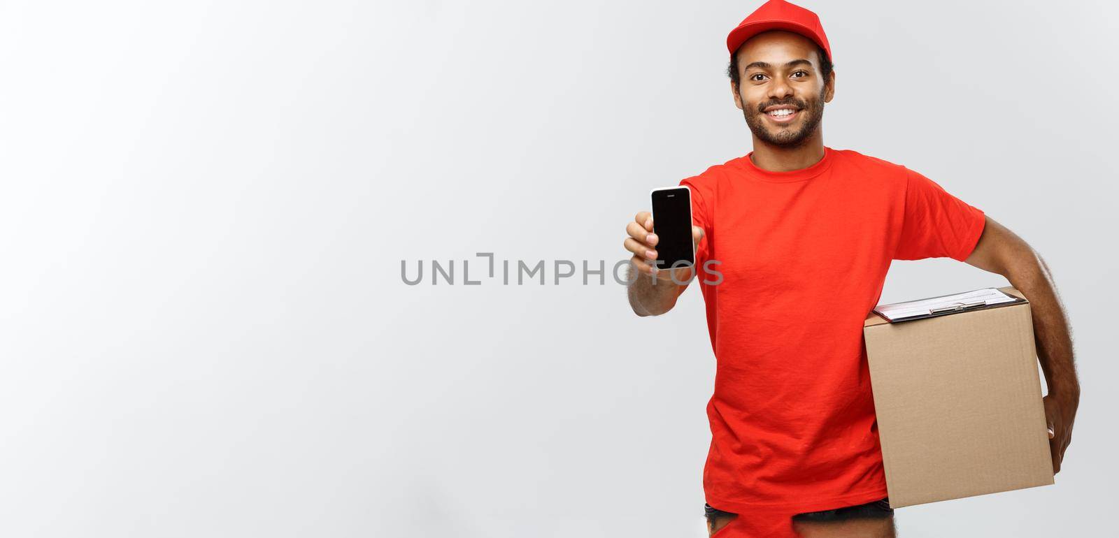 Delivery Concept - Portrait of Handsome African American delivery man or courier with box showing mobile phone on you to check the order. Isolated on Grey studio Background. Copy Space