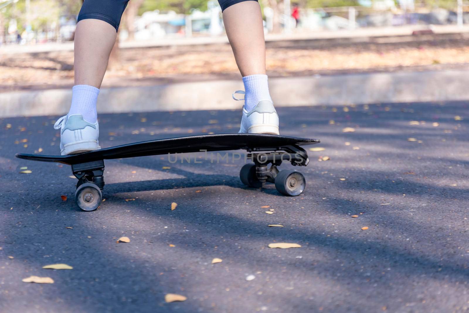 Close-up and motion movement Asian women surf skate or skateboard outdoors on beautiful morning. Happy young women play surf skate at park on morning time. Close up Asian women leg wear sneaker paly surf skate on public park. Sport concept