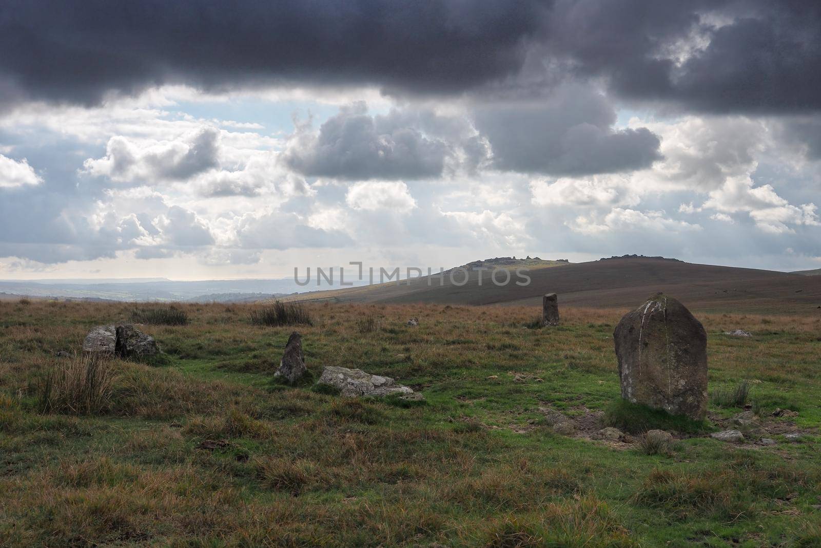 Ancient stone circle under Great Staple Tor with dark cloudy sky overhead, Dartmoor National Park, Devon, UK