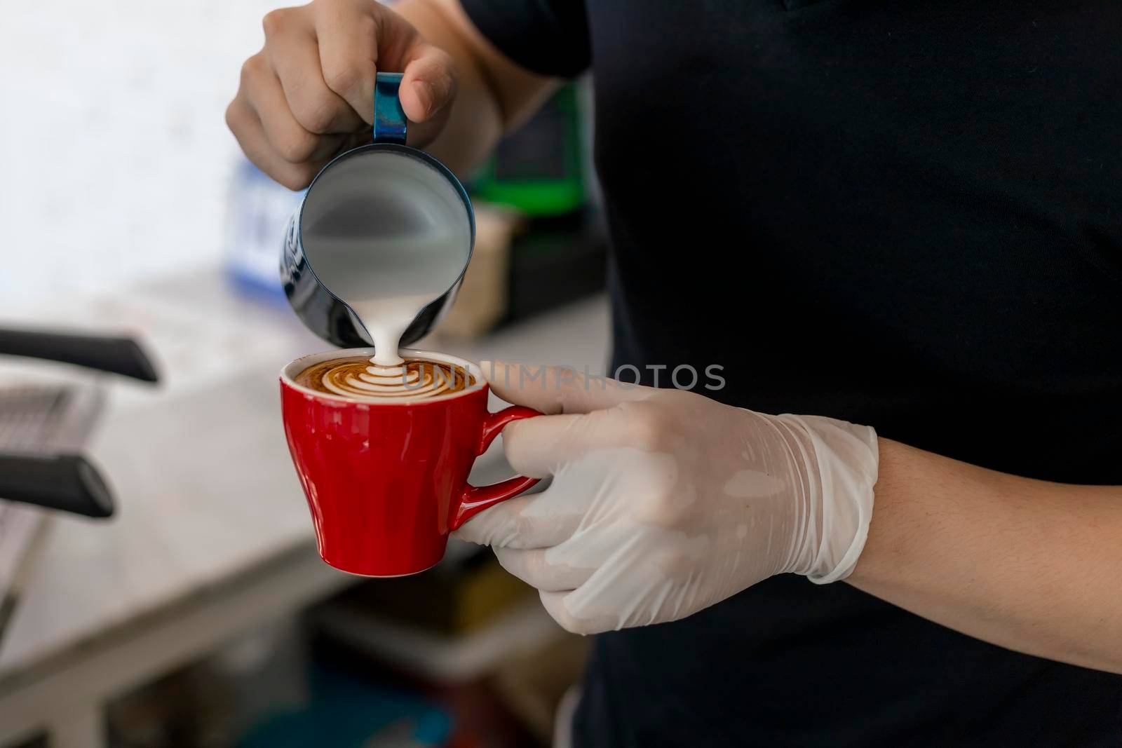 Close up barista pouring steamed milk into coffee cup making beautiful latte, cappuccino art Rosetta pattern. Close up barista hands pouring warm milk in red coffee cup for making latte art.