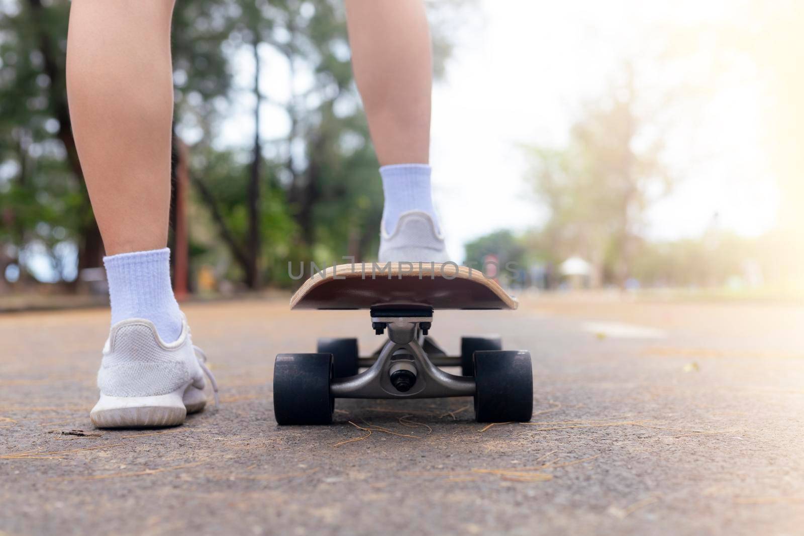 Close up rear view Asian women leg on surf skate or skate board in outdoor Park. Closeup leg wear white sneakers put on surfskate at public park. Extreme sport and relax concept