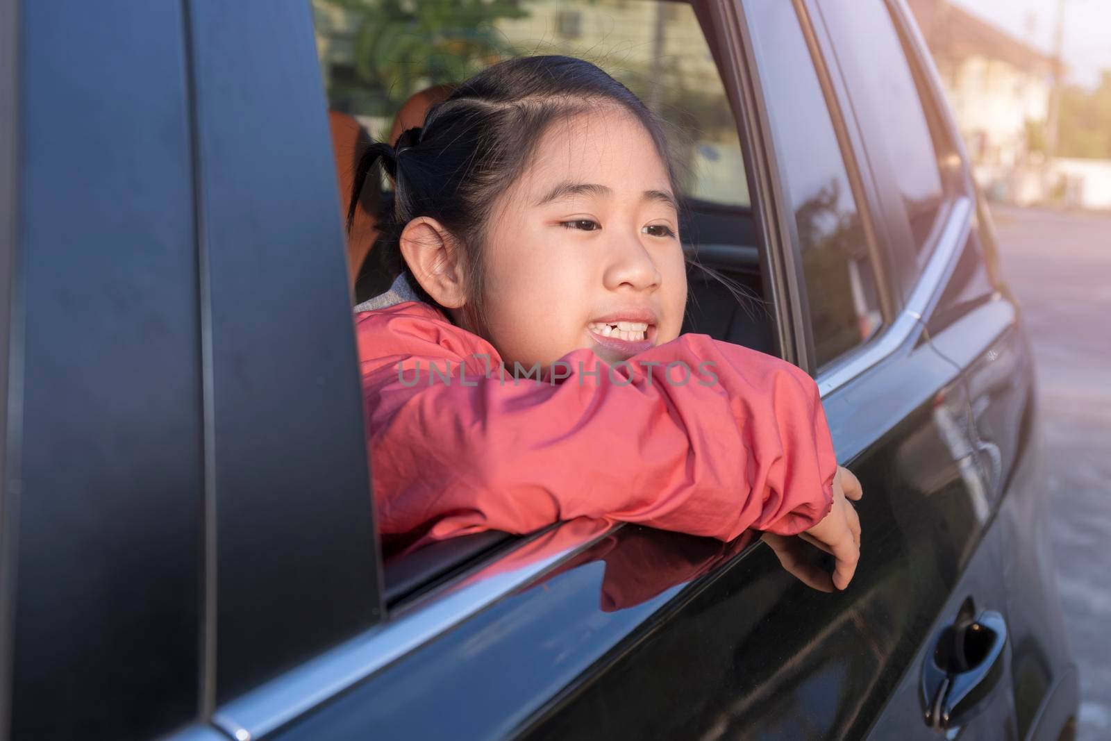 Asian little girl looking something out the car. In the morning, the girl was looking at something outside the car window on the way to school. children relax with street view from the car. Family at car concept. by Satrinekarn