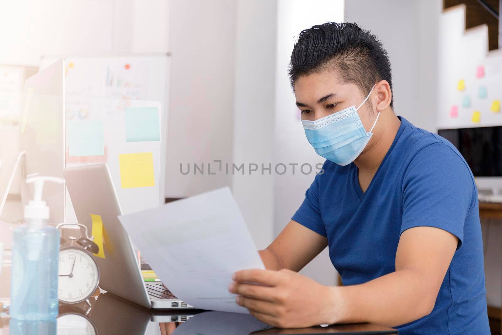 Asian small business start up working at Private Home Office social distancing among Coronavirus outbreak. Businessman wear face mask holding document paper chart .