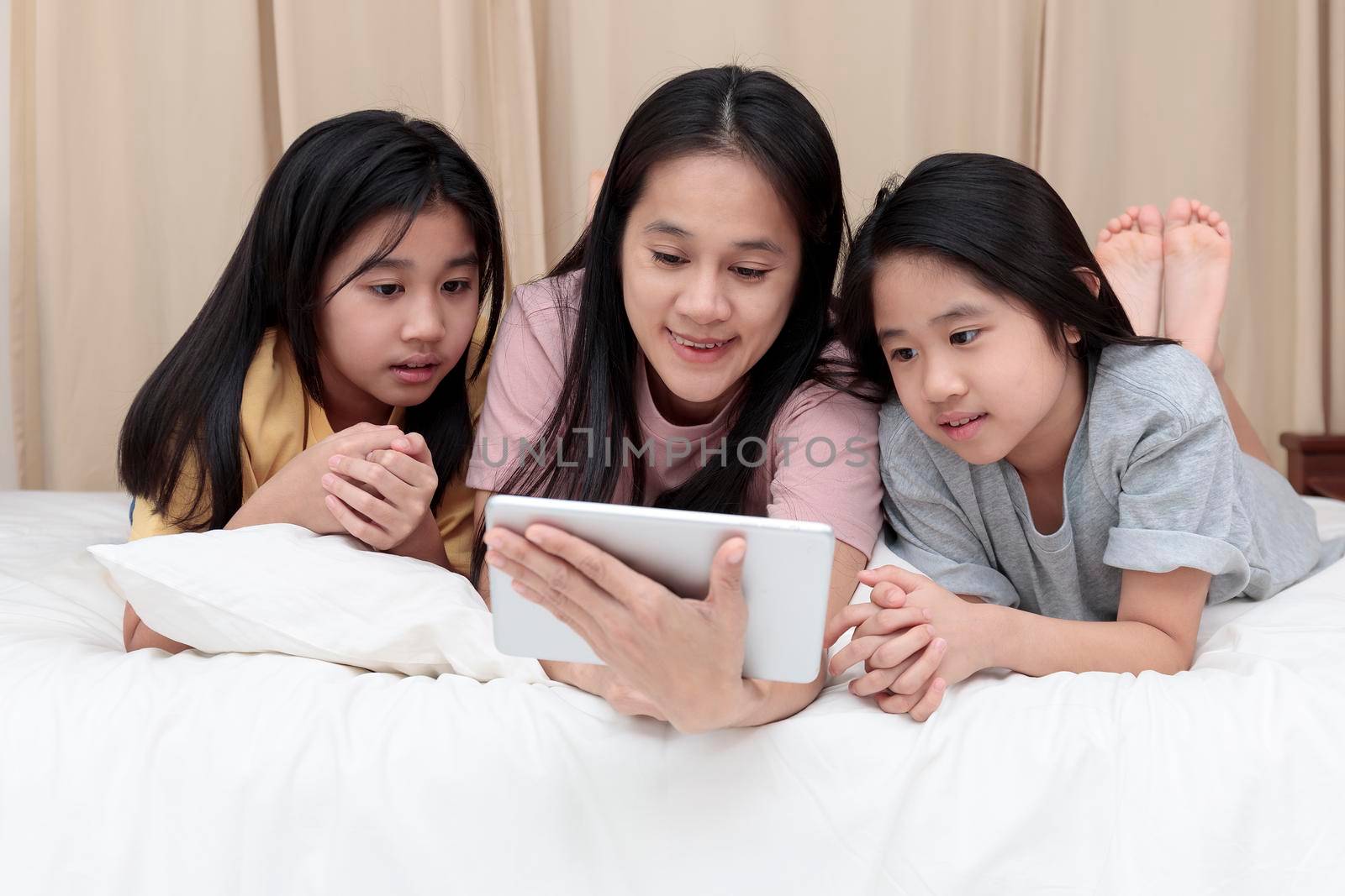 Happy Asian family enjoy and relax on bed in bedroom. mother and daughters enjoy using tablet together on bed.  Family concept.