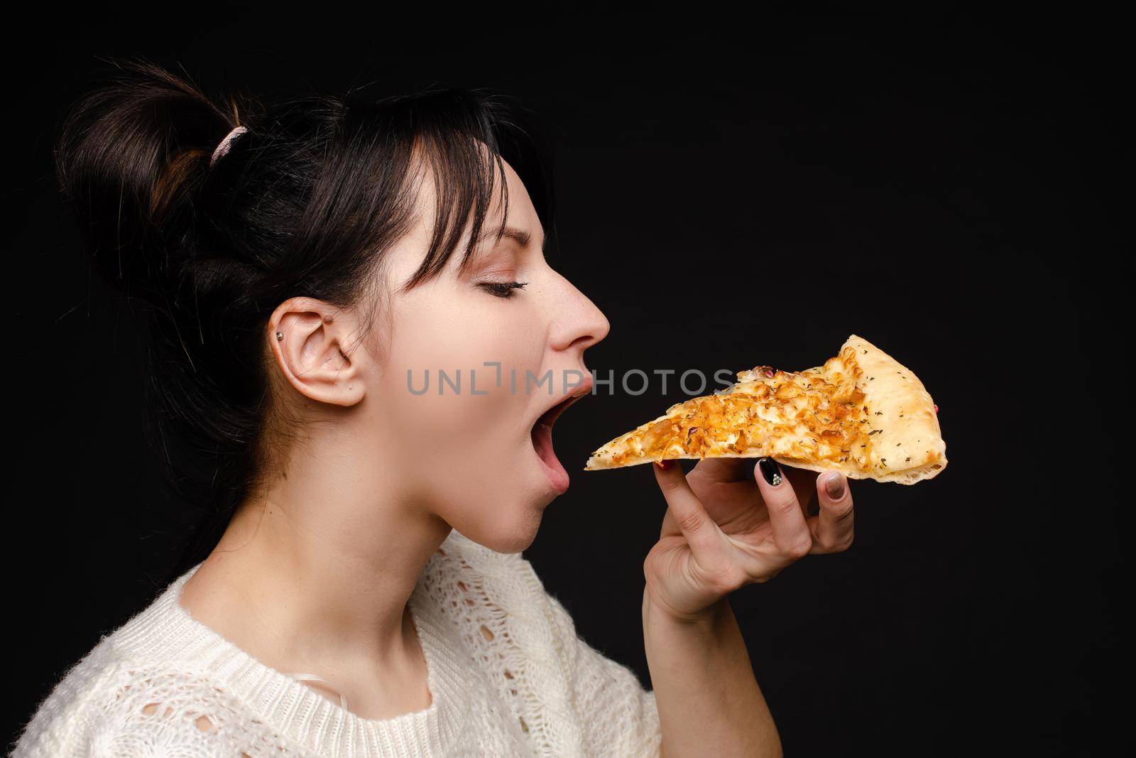 Close-up face of hungry young woman open mouth ready biting appetizing piece of pizza. Casual attractive young female enjoying eating fast food isolated at studio black background side view