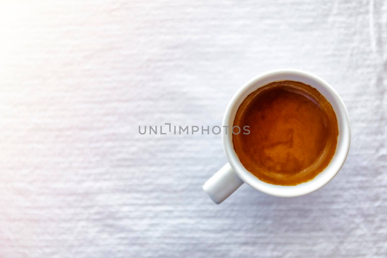 Top view close up of hot espresso coffee in a white ceramic cup on a white tablecloth background on morning