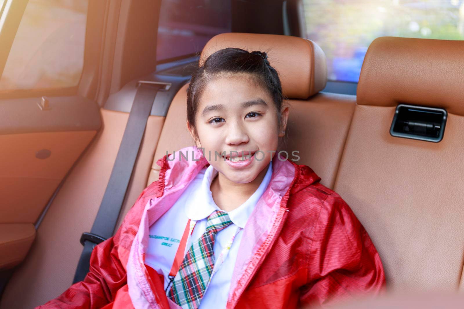 Asian Happy student smiling with camera while enjoying road trip in car. Daughter smiling and looking camera inside car in morning. Asian cildrens sitting in car on the way go to school. Family in car