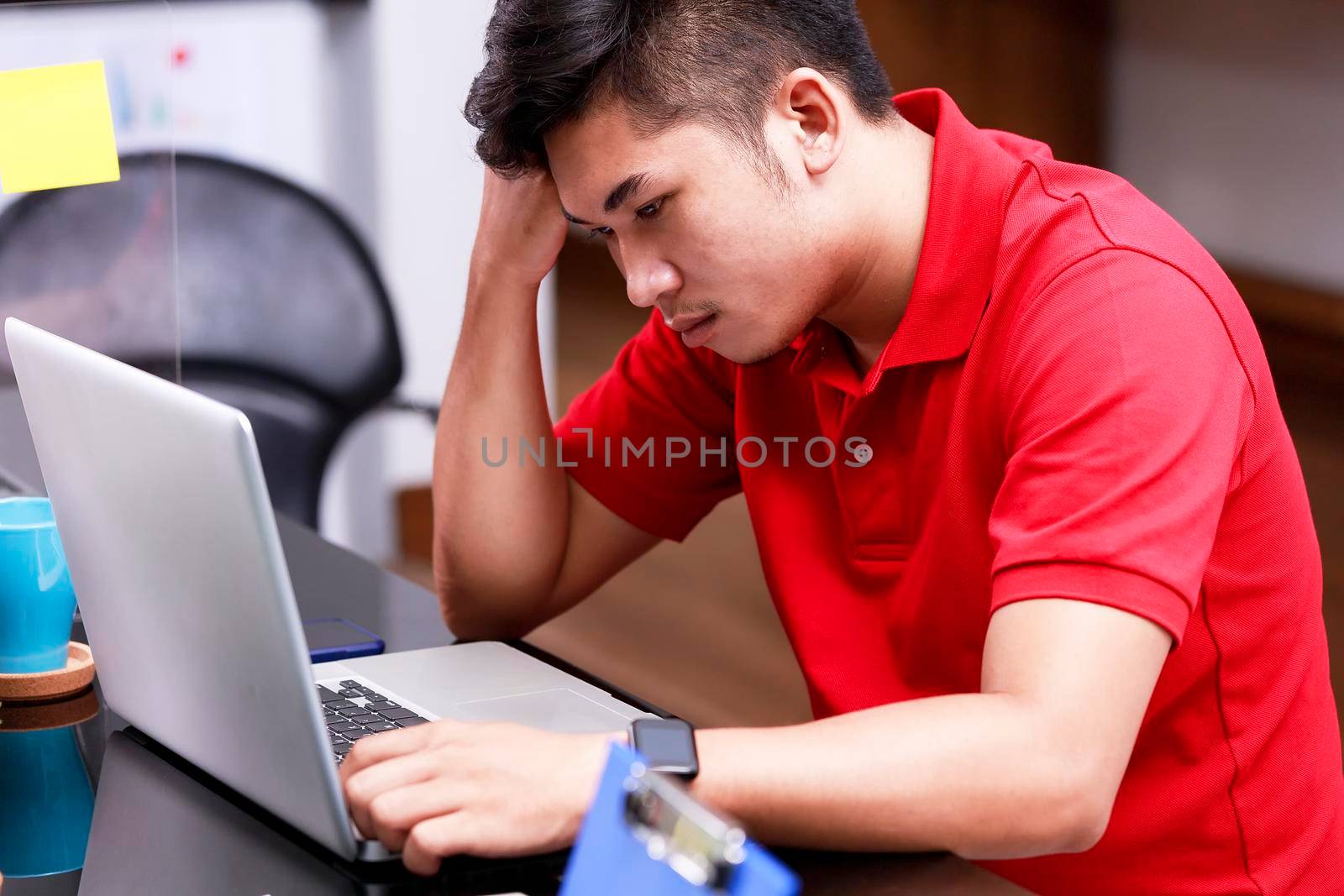 Tired young man worke rfrom headache or migraine at workplace. Male employees have problems from work. Young man having sressful time working on laptop