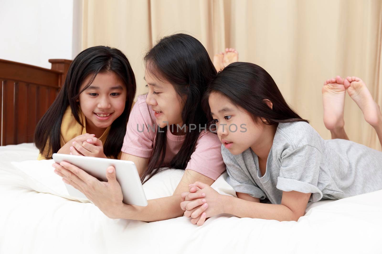 Happy Asian family enjoy and relax on bed in bedroom. mother and daughters enjoy using tablet together on bed.  Family concept.