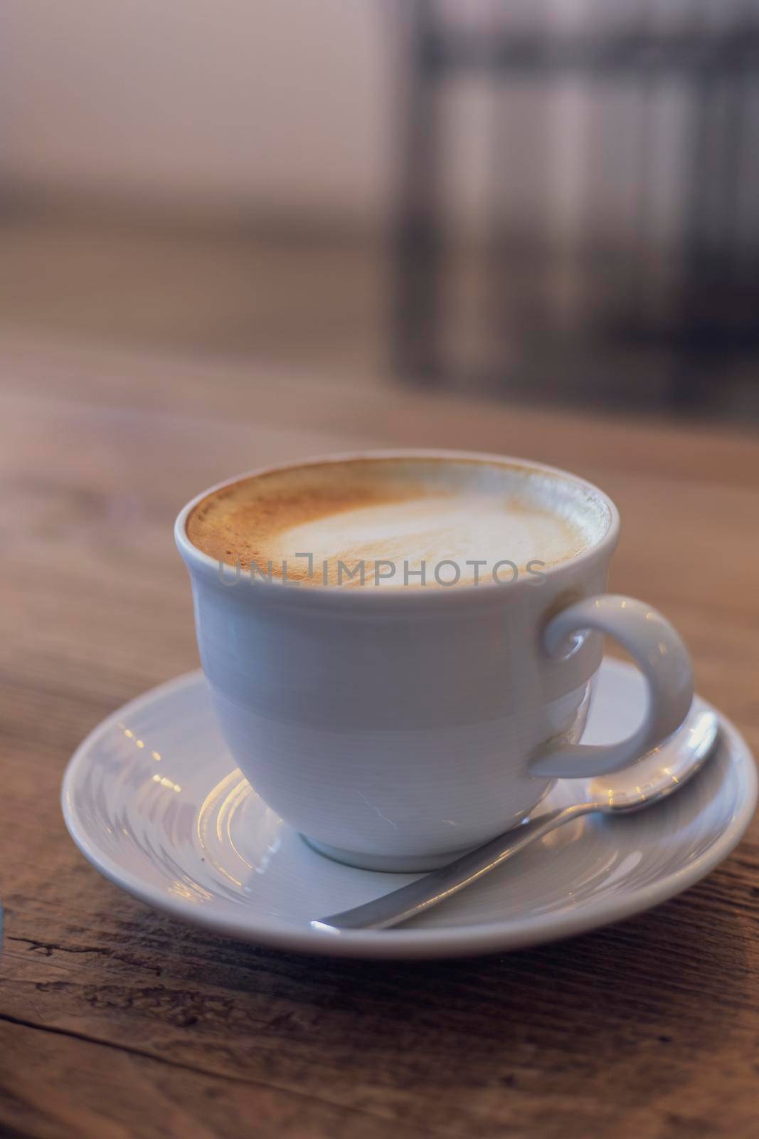 Close up hot cappuccino, latte, caramel macchiato on table with blur coffee shop background. Process with warm vintage tone style. 