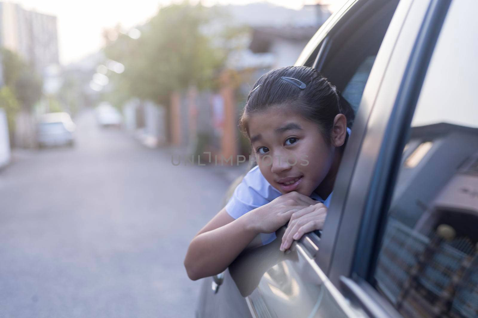 Asian Happy student smiling with camera while enjoying road trip in car. Daughter smiling and looking camera inside car in morning. Asian cildrens sitting in car on the way go to school. Family in car