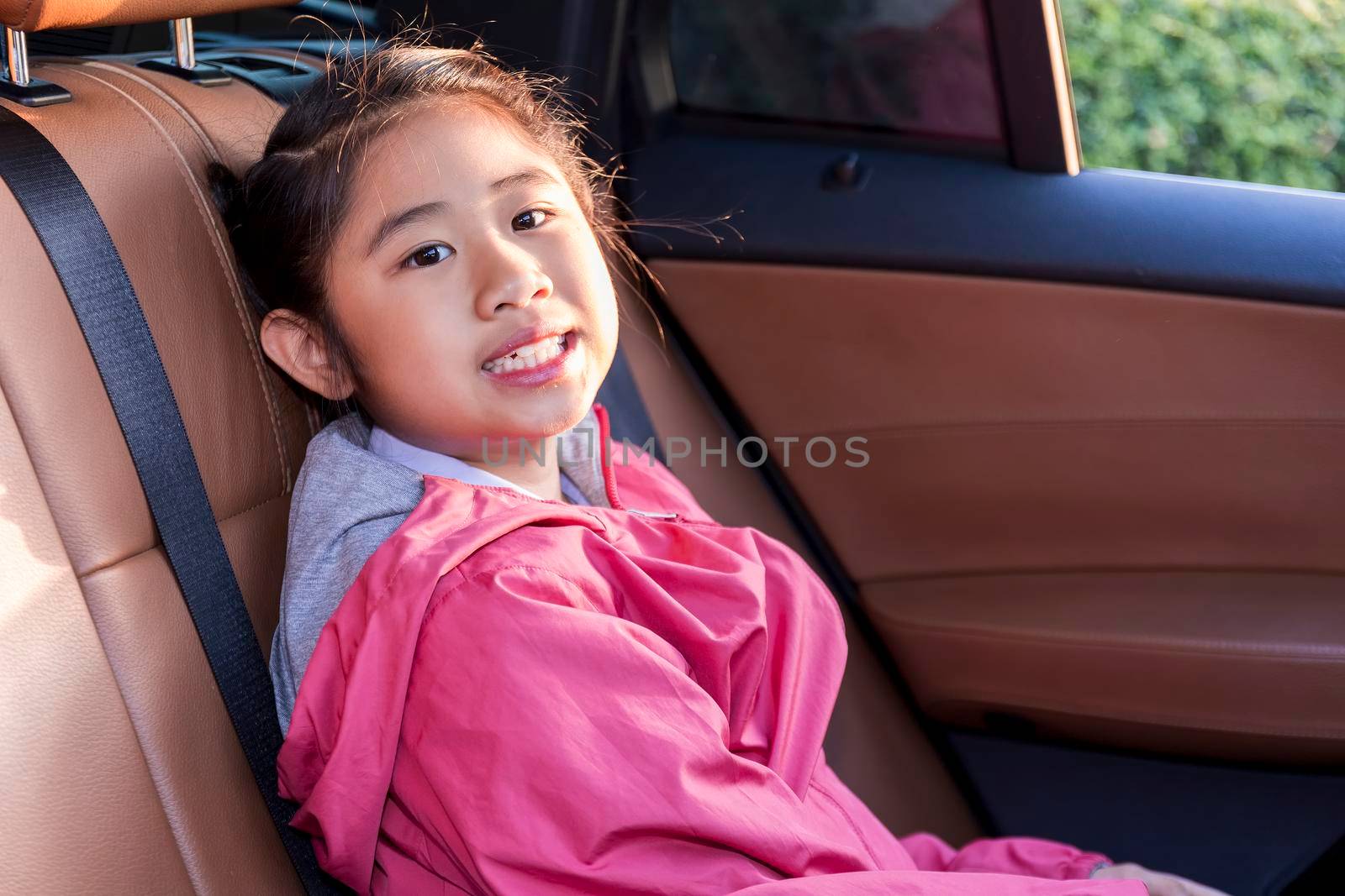 Asian Happy student smiling with camera while enjoying road trip in car. Daughter smiling and looking camera inside car in morning. Asian cildrens sitting in car on the way go to school. Family in car