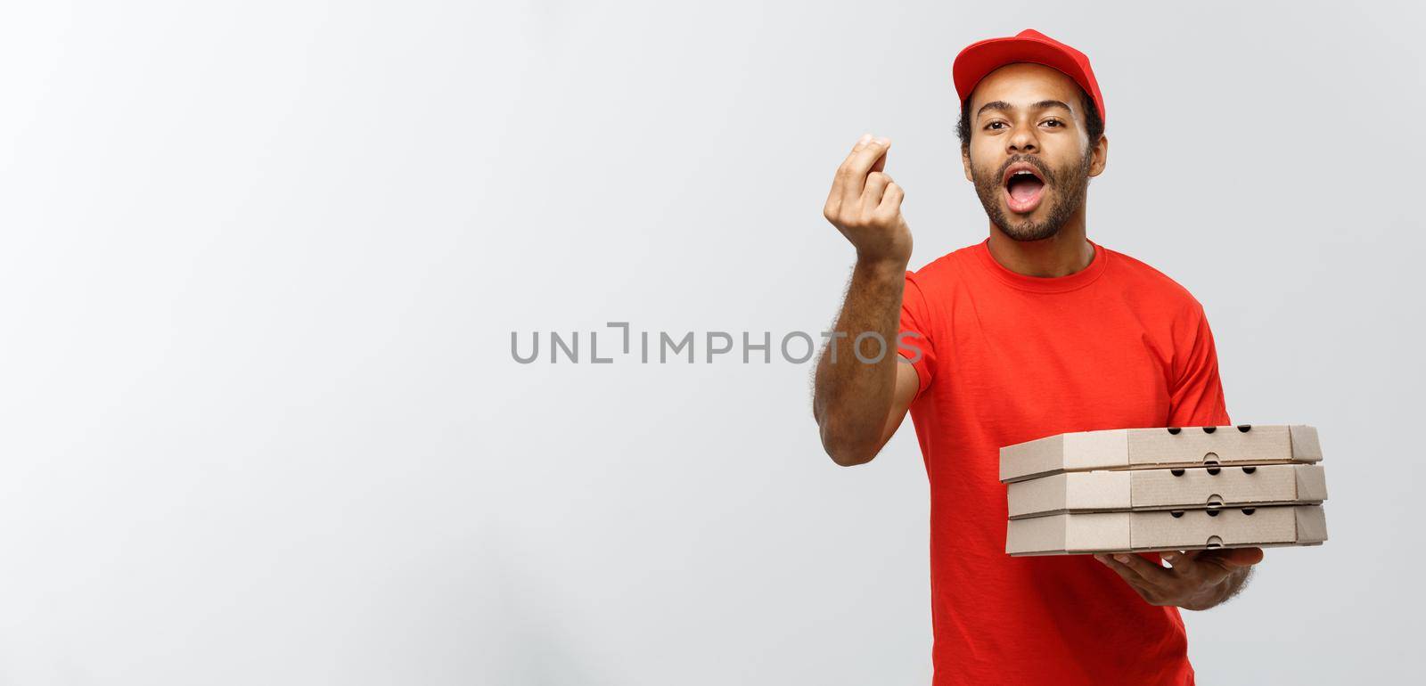 Delivery Concept - Portrait of Happy African American delivery man showing delicious gesture by hand with holding boxes of pizza package. Isolated on Grey studio Background. Copy Space