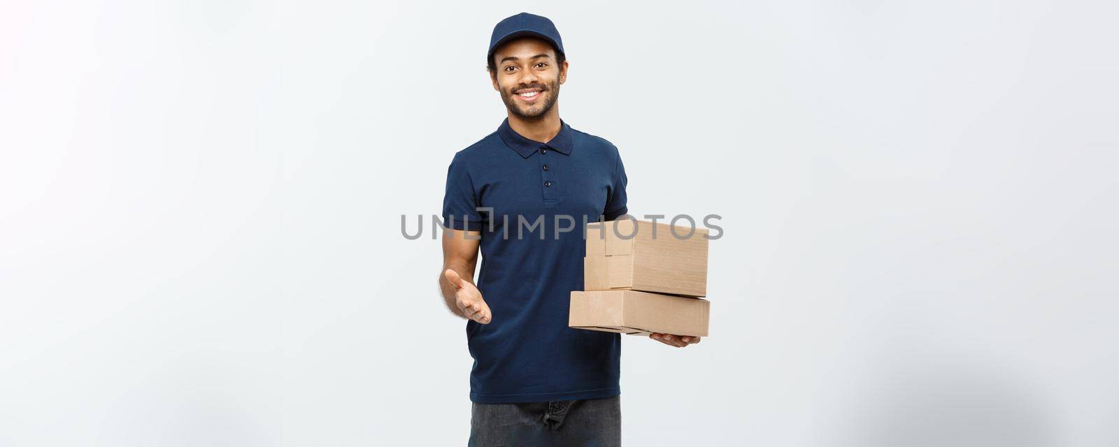 Delivery Concept - Portrait of Happy African American delivery man pointing hand to present box packages. Isolated on Grey studio Background. Copy Space. by Benzoix