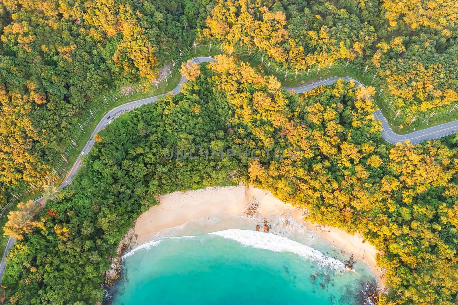 Aerial drone top down view of waves breaking in the sand with road and forest. High angle view of tropical sea with Seafront road. Phuket Thailand curves of coastal road. Phuket is famous tourist destination. Top view traffic road around the beach by Satrinekarn