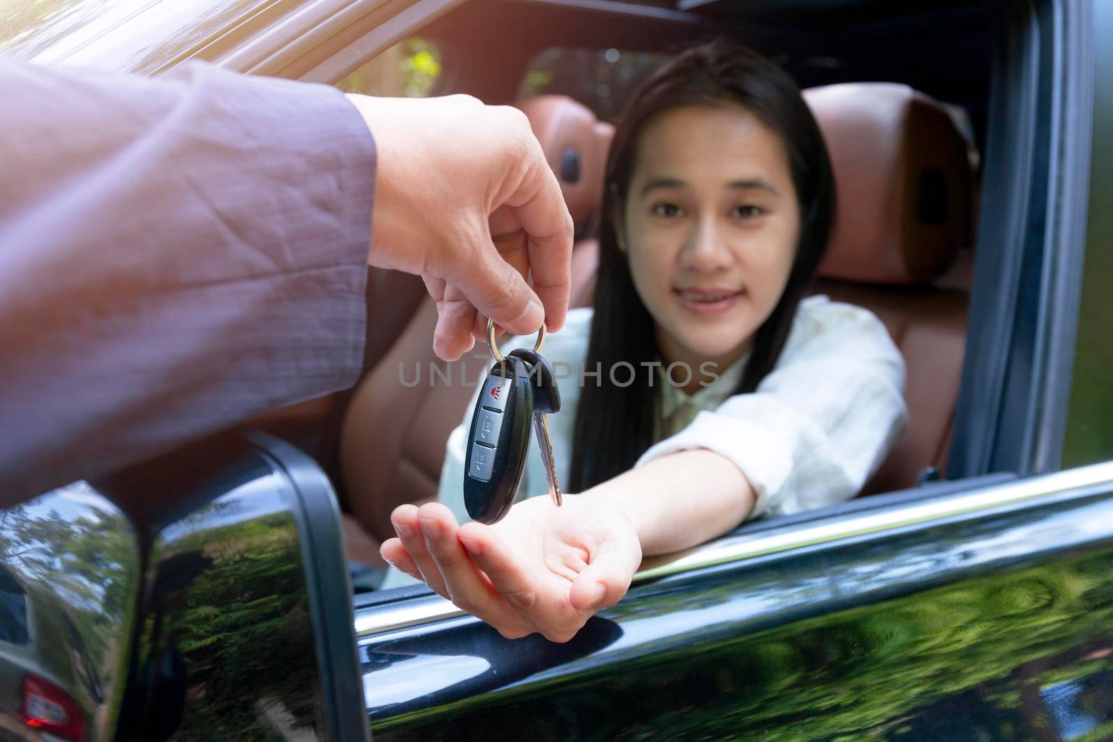 Close up of dealer giving key to new owner car. New car. Auto dealer giving woman automobile key for test drive on country road. Soft focus  smiling women try to test drive a car on road with dealer. by Satrinekarn