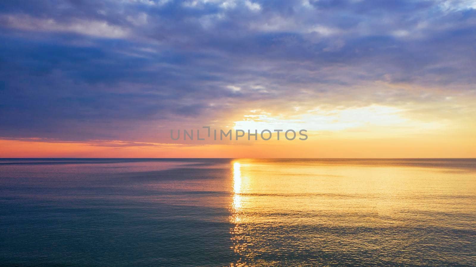 Beautiful sunset over the clam sea with cloud and sky background. Sunset over tropical beach. Nature summer  concept. Peak sunset over sea with yellow light reflect in cloud.