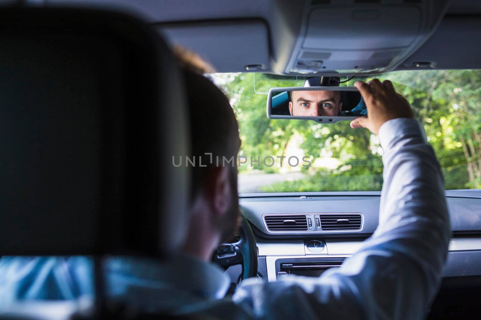 man sitting inside car adjusting rear view mirror