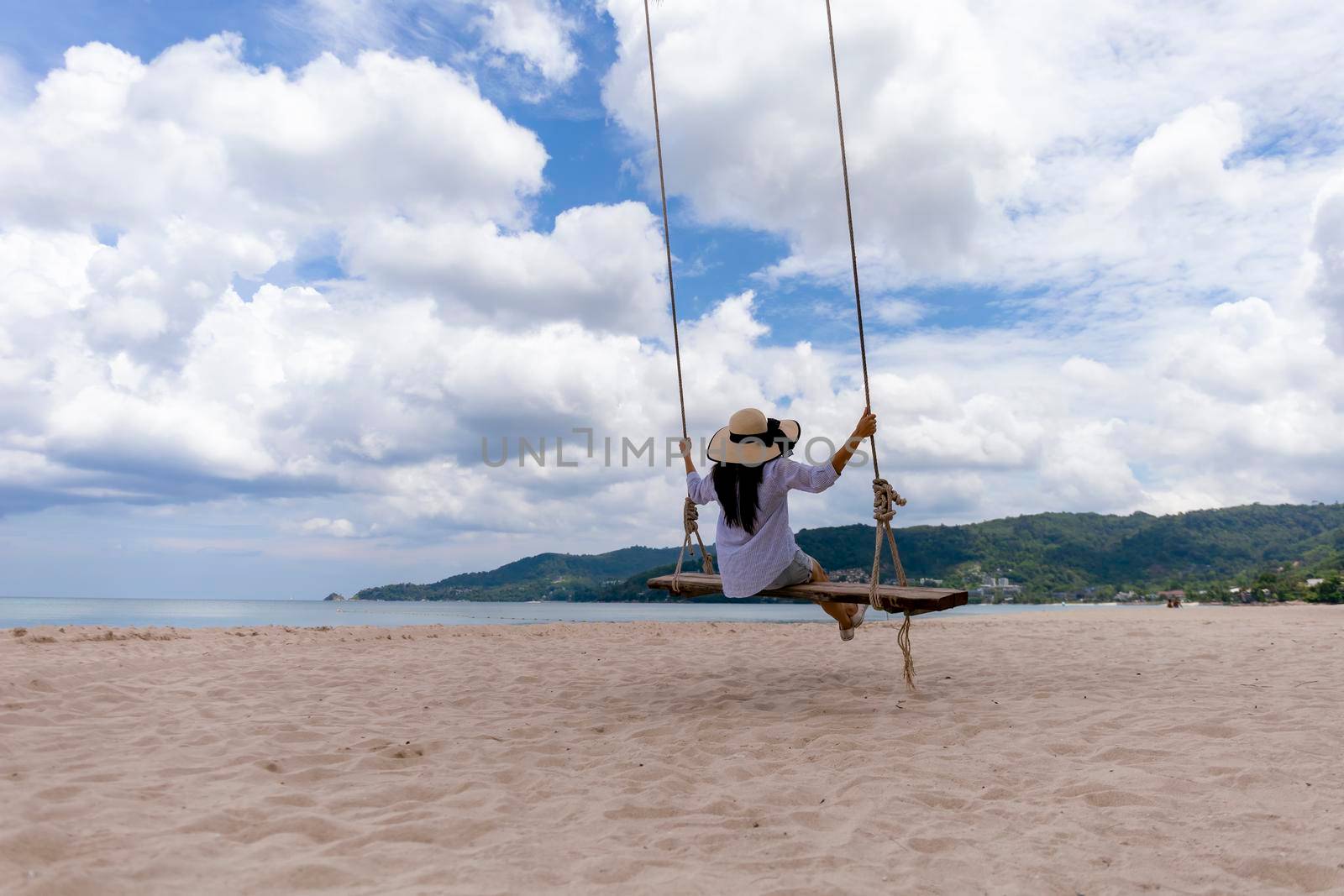 Phuket, Thailand. Tropical beach paradise with beach swing with girl in white shirt. Women relax on swing under coconut palm tree at beautiful tropical beach White sand. Luxury beach scene vacation summer holiday concept.
