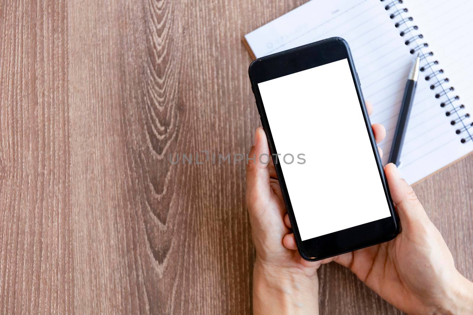 Top view female hands holding smart phone with blank white screen. Women hands workspace, close-up hand holding smartphone blank screen for text and content on wood table background.