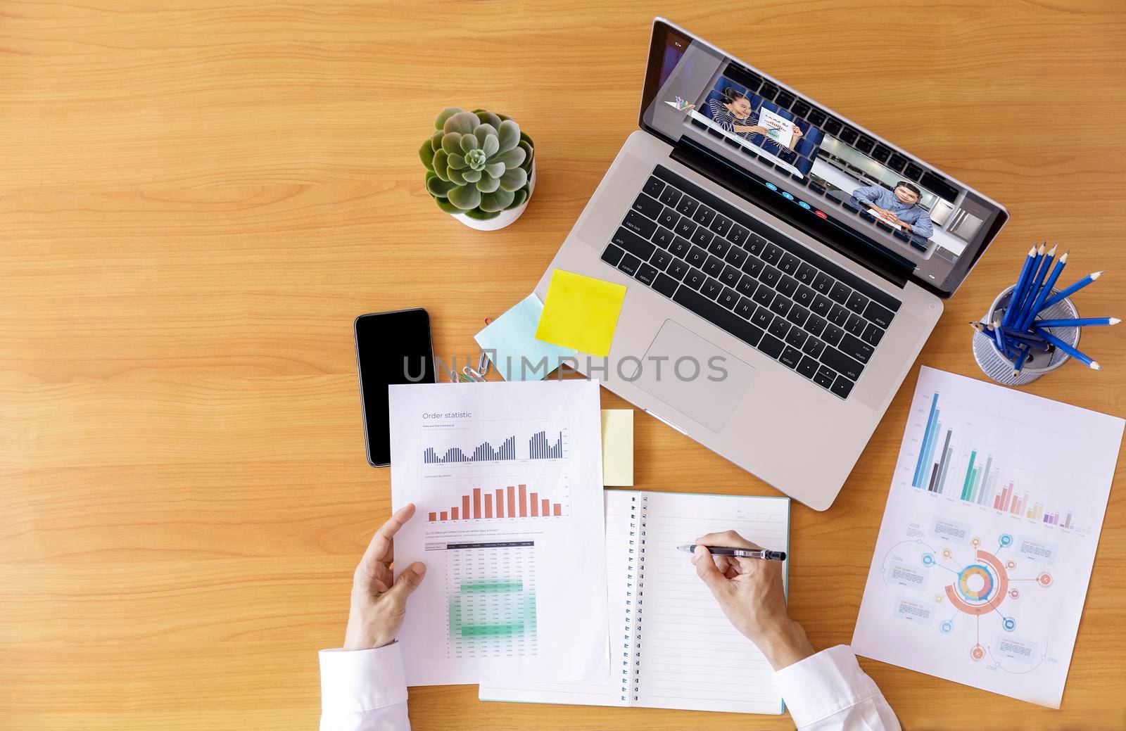 Top view Businessman and businesswoman analysis financial chart with videoconference online meeting. Hand of businesswomen using laptop meeting with diverse colleagues. Covid-19 working from home. With copy space banner by Satrinekarn