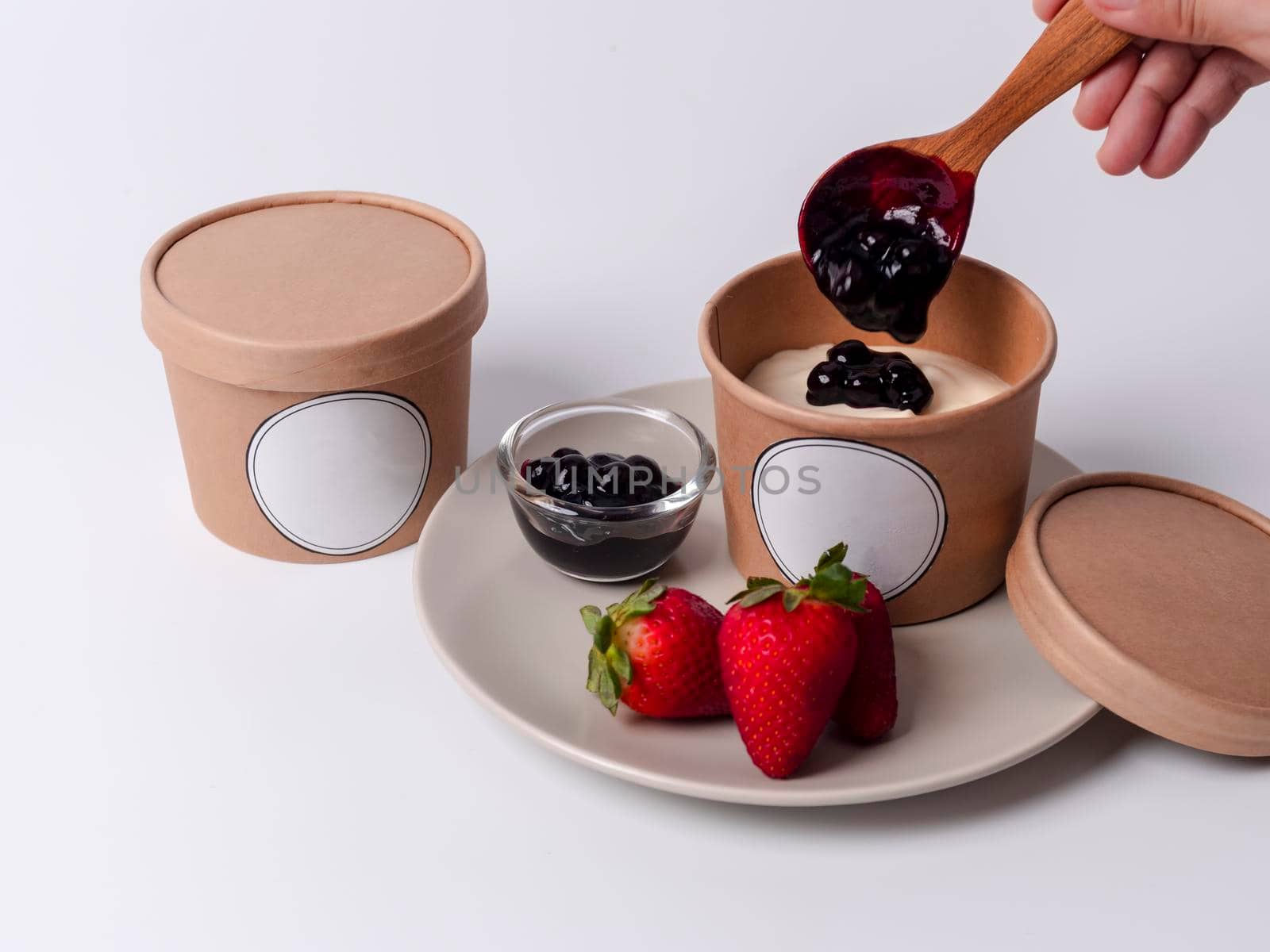 Hands of pastry chef hold wood spoon drop blueberry sauce on  cheese pie in paper craft cup with empty label. Homemade blueberry cheese cake in paper cup.