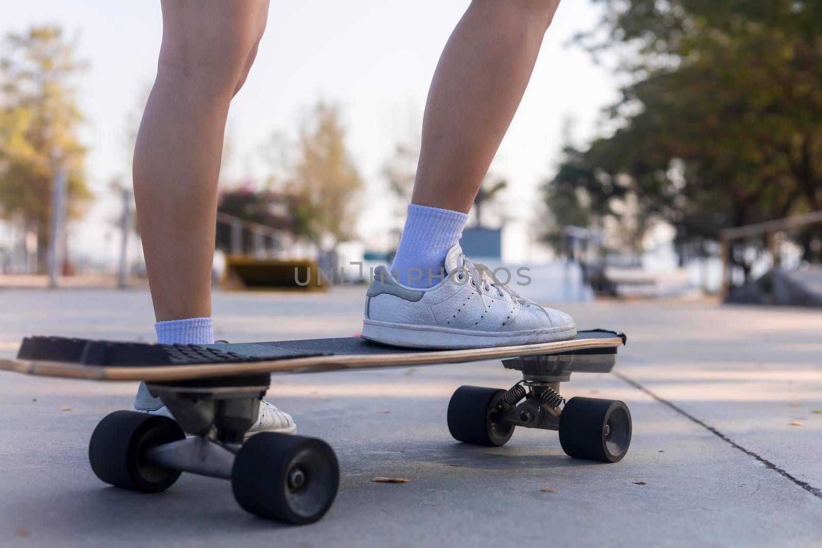 Close-up Asian women surf skate or skateboard outdoors on beautiful morning. Happy young women play surf skate at ramp park on morning time. Close up Asian women leg wear sneaker play surf skate 